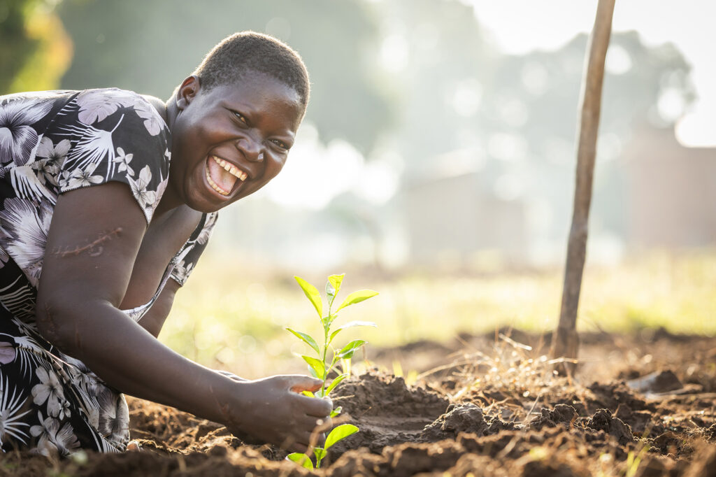 Double the difference donation impact - female farmer looking at camera and smiling next to a plant