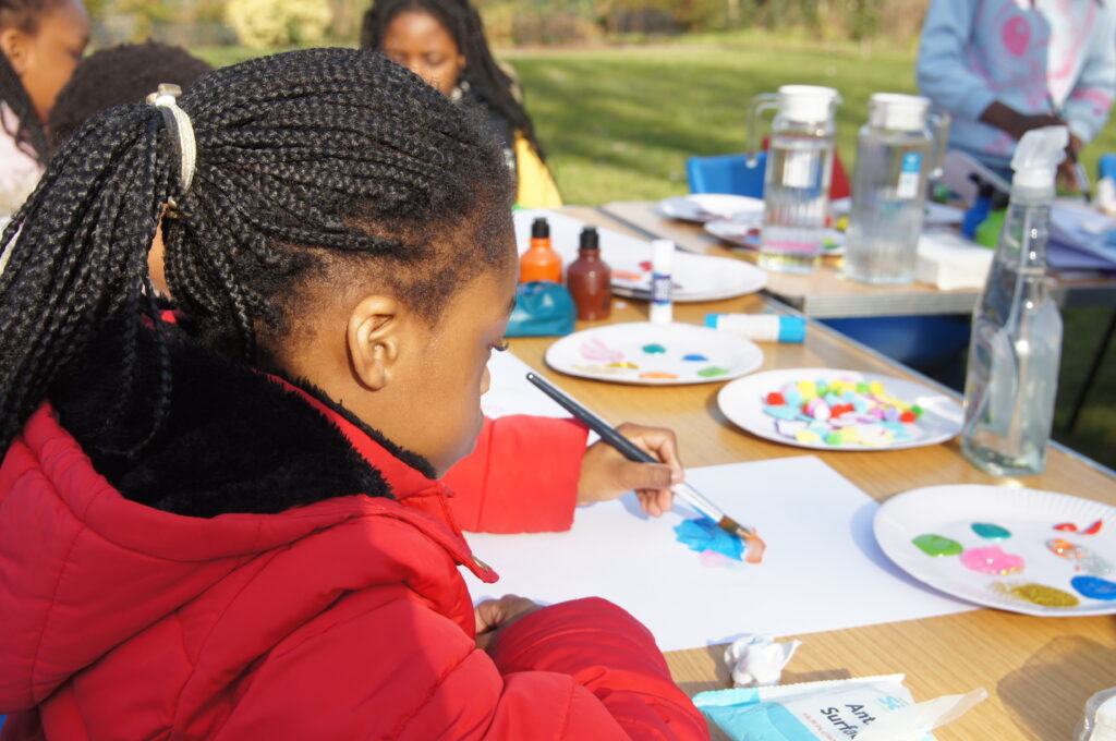 Double the difference donation impact - child in red coat painting on paper