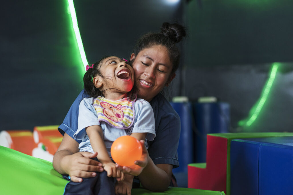 Double the difference donation impact - child in support worker's lap, holding orange ball and smiling